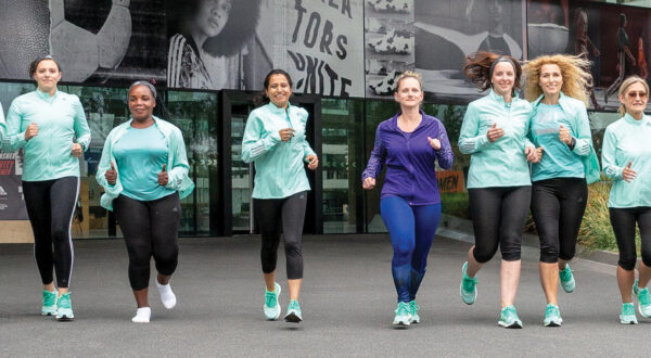 A line of women dressed in aqua and purple running down a city street \ 261 Fearless