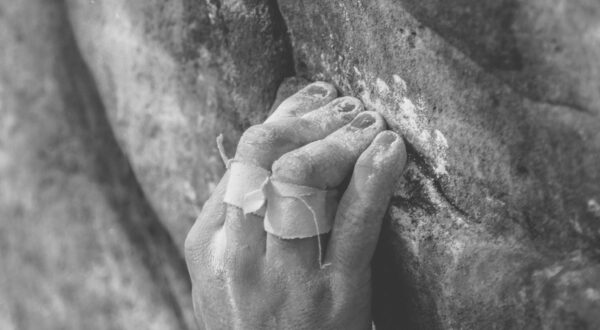 Black and white photo of taped fingers gripping rock ledge while climbing