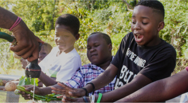 Three Black children smiling while washing vegetables harvest from Jones Valley Teaching Farm
