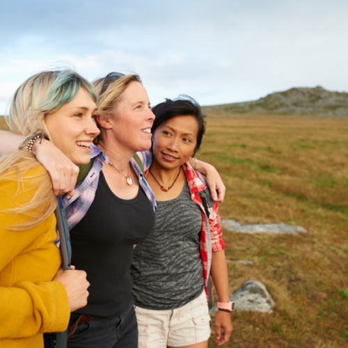 Three women arm in arm standing on a mountain. Find Your Good