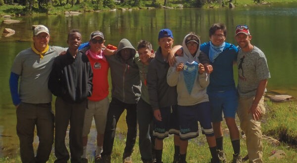A group of kids standing in front of a lake and trees and mountains | Big City Mountaineers