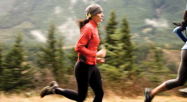 Two women running on a dirt path with mountain in background