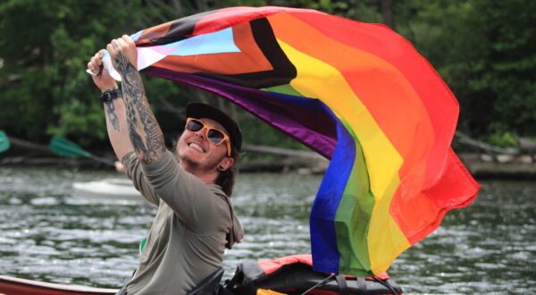 Smiling person in kayak holding pride flag overhead